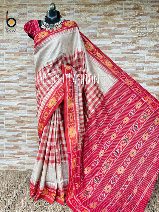 A red and beige striped silk saree with a red border featuring yellow and orange motifs, draped on a black mannequin with a red embroidered blouse. The background is a beige stone-tile wall.